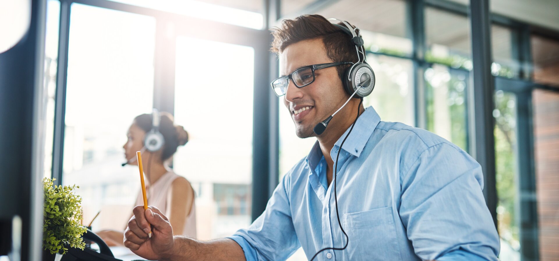 © iStock-1132874986_PeopleImages (Cropped shot of a handsome young man working in a call center with a female colleague in the background)